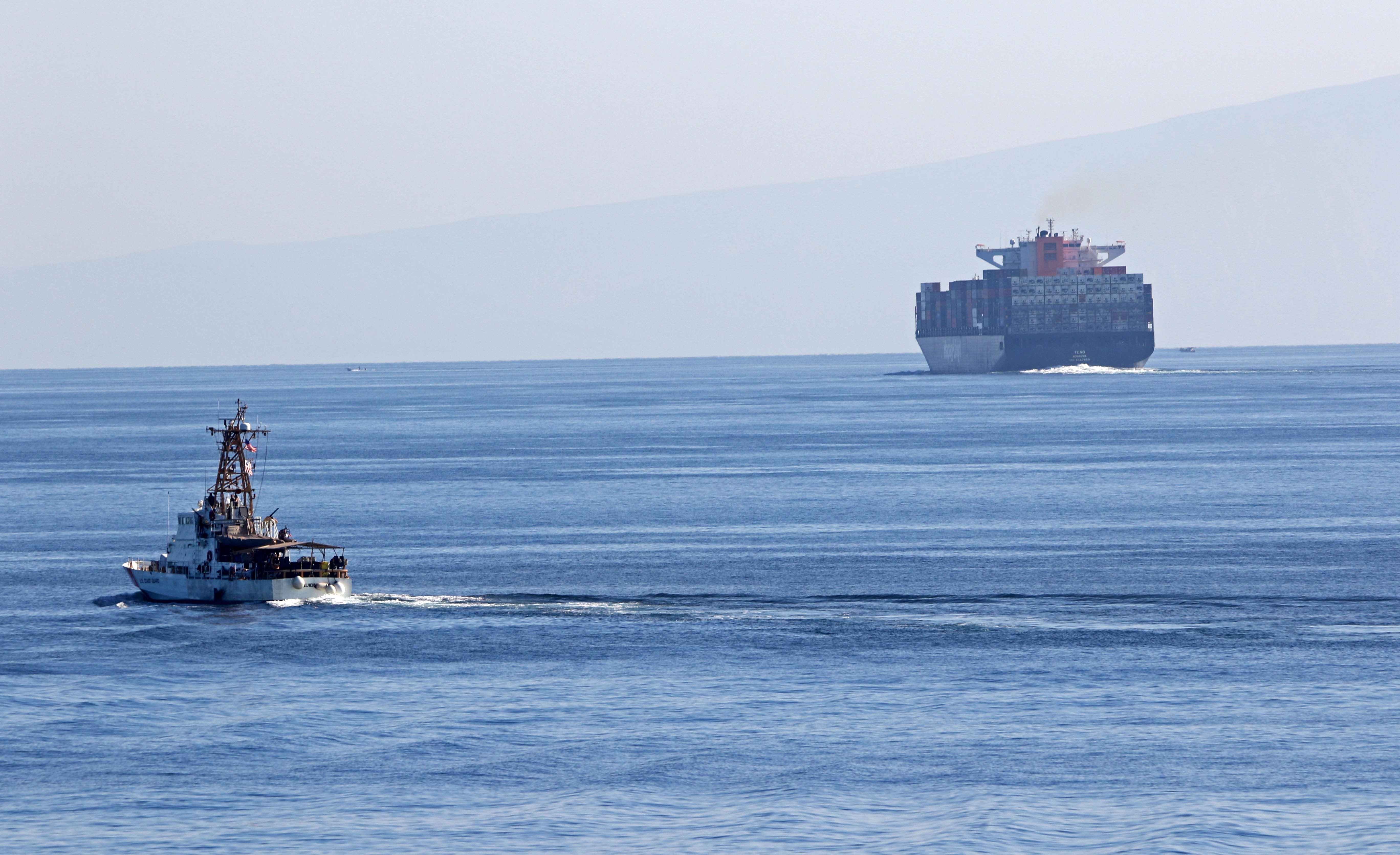 A Coast Guard cutter and a container ship transit the Strait of Hormuz